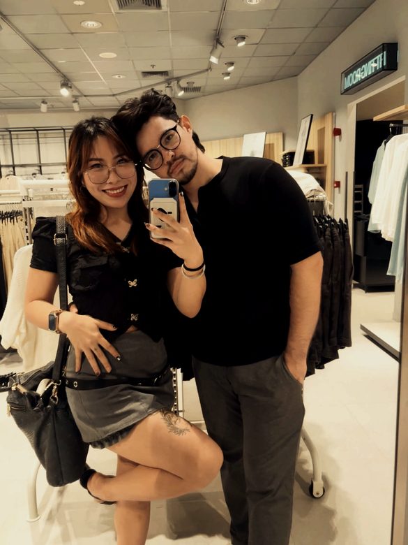 Marc-Kevin and Florence in a clothing shop, both in black, taking a mirror photo.